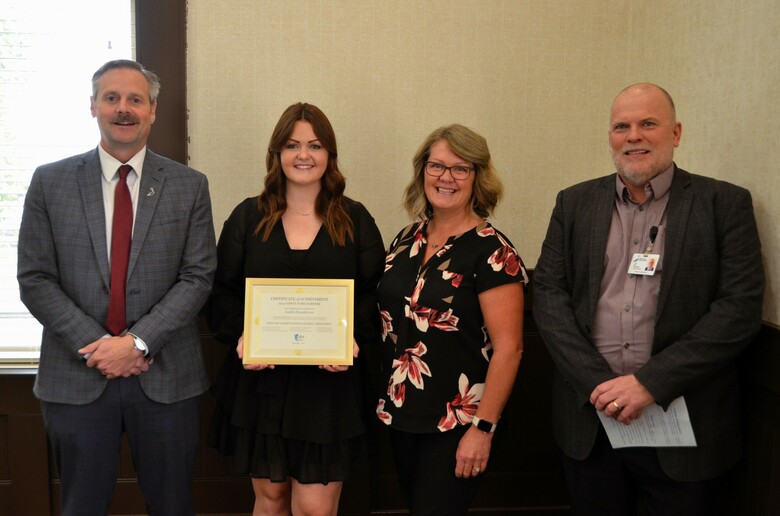 PRSD Superintendent Adam Murray (white male, grey suit, red tie) and Deputy Superintendent Jeff Thompson (white male, black suit, purple shirt) stand with the PRSD's Edwin Parr nominee Kaitlin Saunderson (white female, mid-20s, black dress, long brown hai